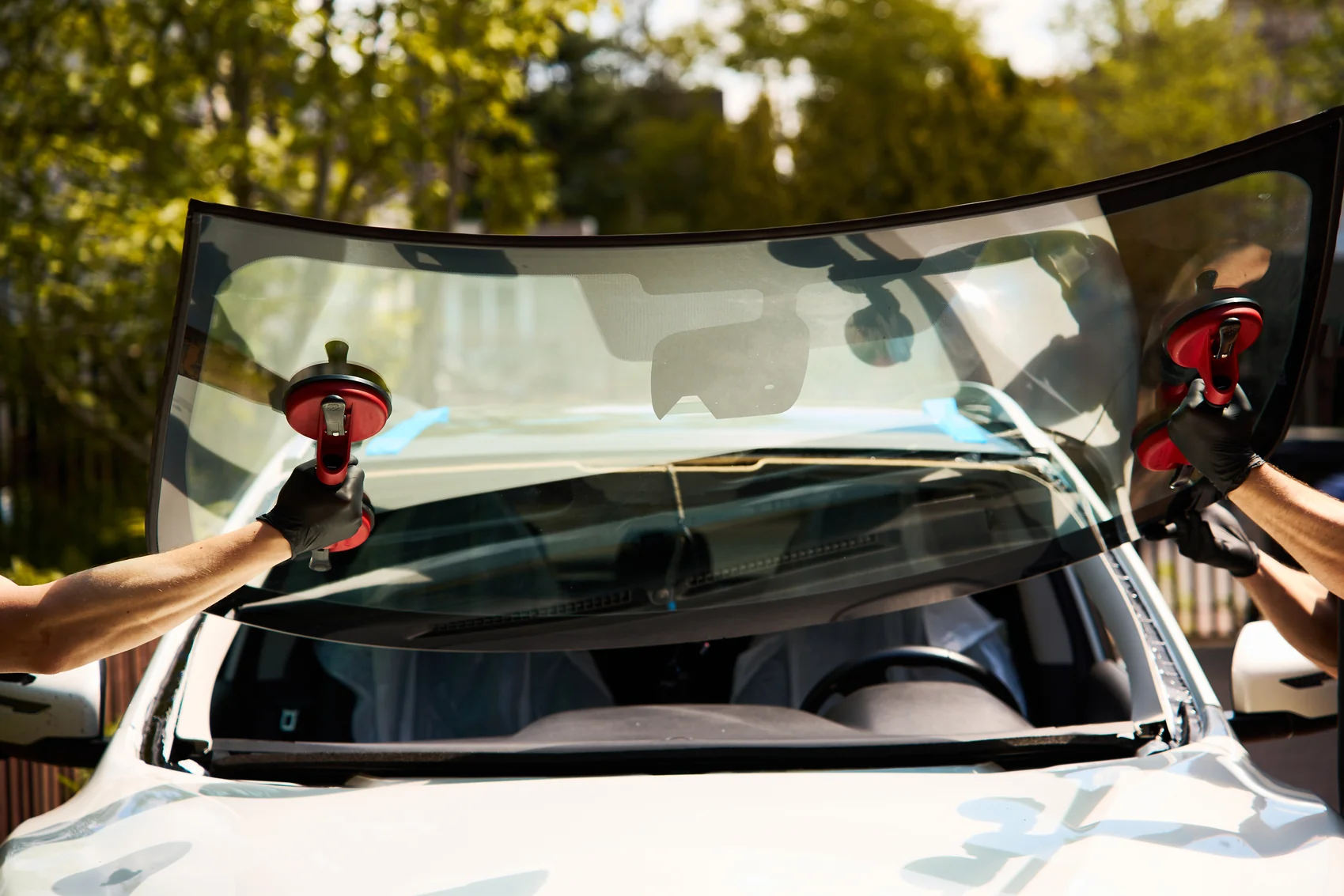 Two auto glass technicians using suction cups to set a new windshield on a car