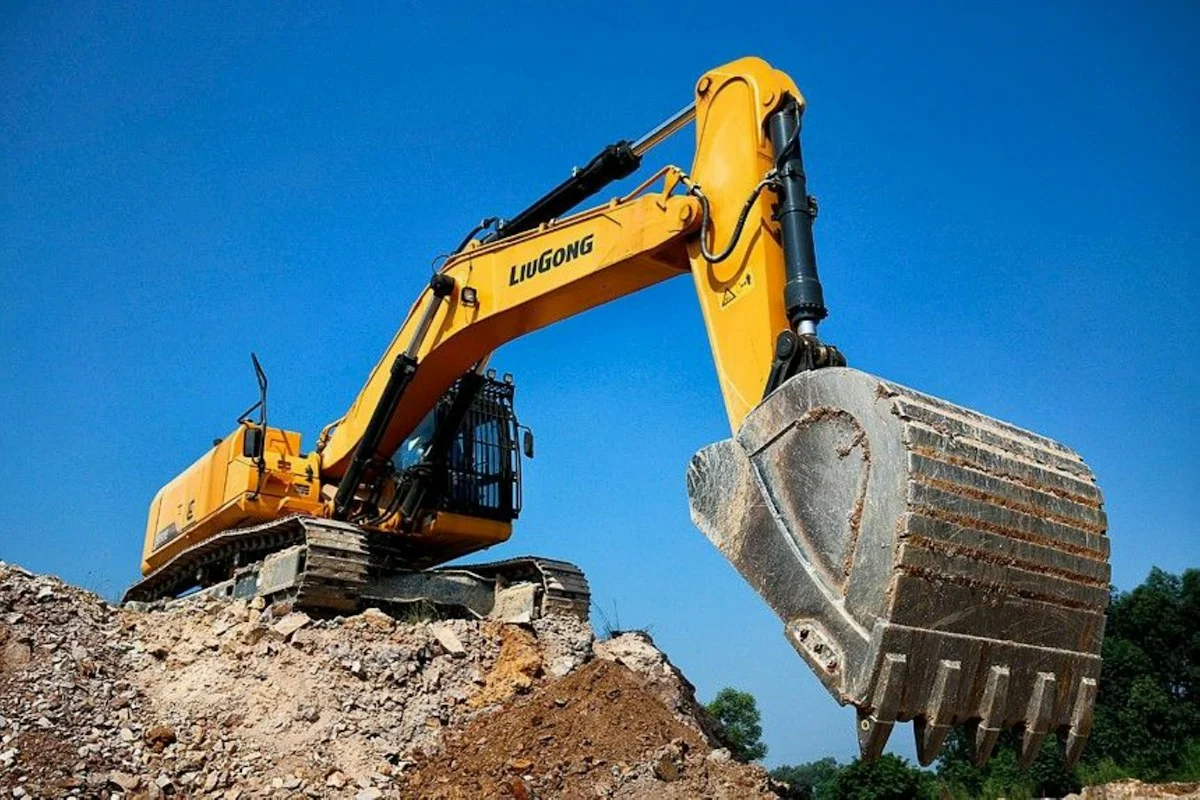 Yellow excavator digging dirt on a construction site against a blue sky