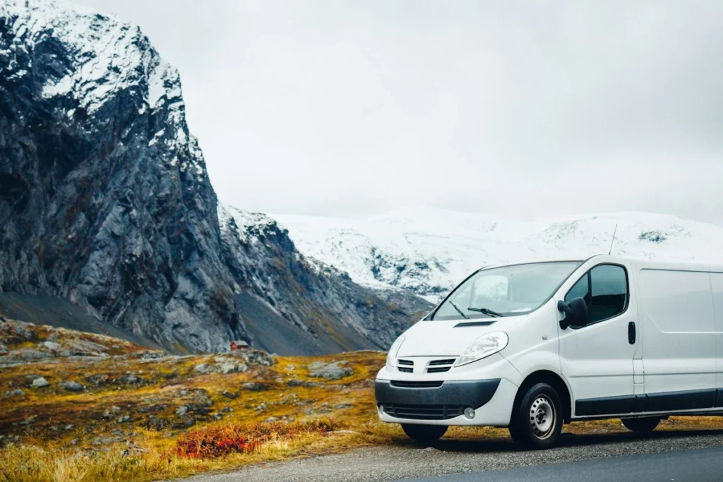 White work van parked on a mountain road below snowy peaks